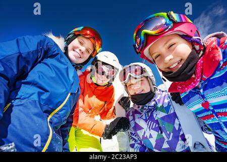 Gruppo di bambini in maschera da sci e caschi ang guardare giù in piedi insieme sopra il cielo blu Foto Stock