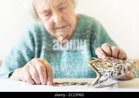 In questione anziani 96 anni vecchia donna seduta a tavola in casa e il conteggio delle monete rimanenti dai regimi pensionistici nel suo portafoglio dopo il pagamento di fatture. Unsustainabi Foto Stock