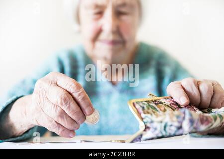 In questione anziani 96 anni vecchia donna seduta a tavola in casa e il conteggio delle monete rimanenti dai regimi pensionistici nel suo portafoglio dopo il pagamento di fatture. Unsustainabi Foto Stock