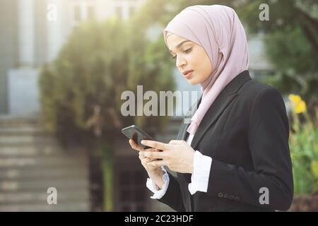 Musulmani donna di affari e a piedi utilizzando smart phone. Foto Stock