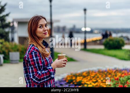 Caffè sul andare. Bella giovane donna azienda tazza da caffè e sorridente nel parco Foto Stock
