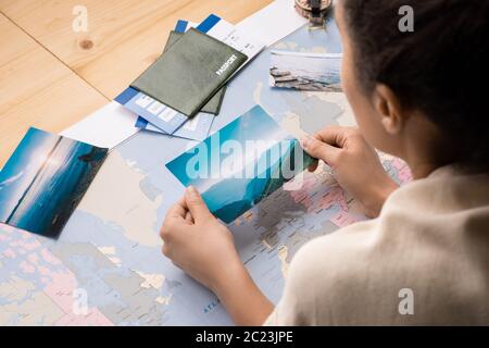 Vista a spalla di una donna che si appoggia al tavolo con la mappa del mondo e guarda le foto mentre sogna il viaggio Foto Stock