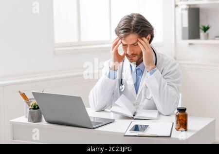 Medico stressato che soffre di mal di testa sul posto di lavoro Foto Stock