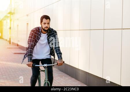 Considerato bello uomo barbuto in eleganti vestiti in sella ad una bicicletta su strada, all'esterno. Foto Stock