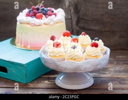 Torta rosa con cioccolato fuso, fragola, mirtillo e ciliegia e cupcake con panna montata e frutti di bosco freschi. Foto Stock