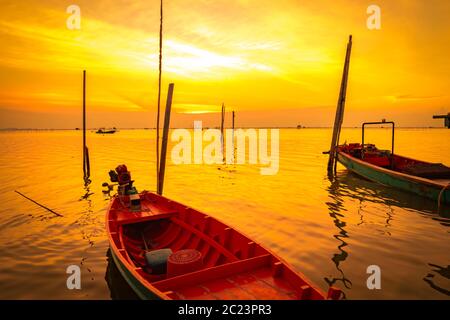 La barca dei pescatori galleggia in mare vicino al palo di bambù al tramonto in Thailandia. Foto Stock