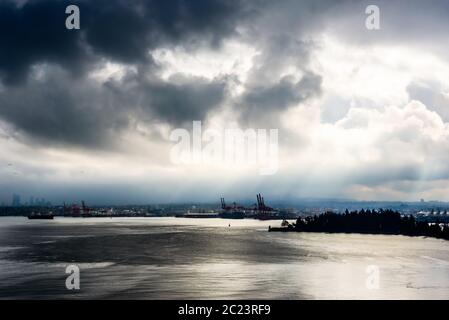 Rottura sole attraverso da dietro le nuvole scure in alto contrasto su acqua in Vancouver, British Columbia, Canada. Foto Stock