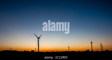 Silhouette nera di diverse turbine eoliche contro arancione e il blu del cielo al crepuscolo. Foto Stock