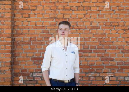 Ritratto di un vestito casualmente giovane imprenditore in piedi contro un muro di mattoni Foto Stock