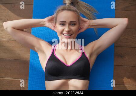 Fitness determinata donna di mezza età mentendo facendo crunches a casa su tappetino palestra Foto Stock