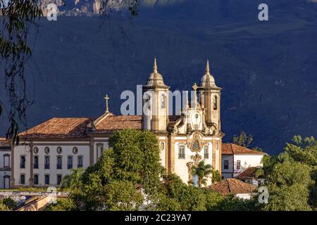 Antica chiesa cattolica storica e colline nel basso della città di Ouro Preto Foto Stock