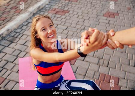 Voce maschile consente una bella donna fitness ad alzarsi dopo aver fatto un esercizio di sport sul tappeto. Uno stile di vita sano. Foto Stock