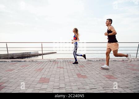 Vista laterale del giovane sportivo, jogging sul quay, correre una maratona, vicino all'oceano. Sport concept. Foto Stock