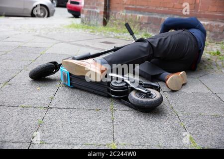 Inconscio uomo disteso sul cemento Street dopo un incidente con uno scooter elettrico Foto Stock