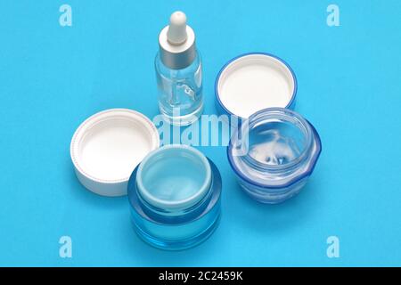 Aprire i vasetti di creme cosmetiche e sieri su sfondo blu Foto Stock