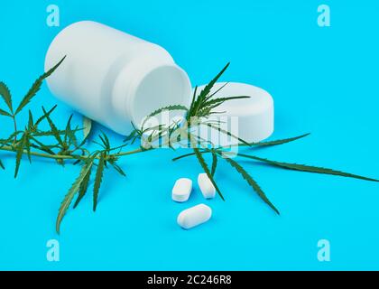 La cannabis ramo con foglie di colore verde e bianco vaso in plastica con le compresse di forma ovale su uno sfondo blu, concetto di legalizzazione di trattamento alternativo Foto Stock