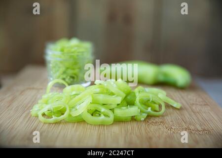 Freschi fette di banana peperoni su un tagliere con i jar pronto per il decapaggio. Foto Stock