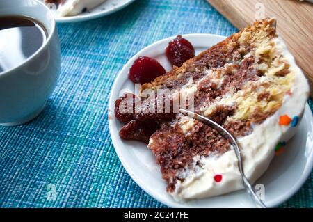 Un pezzo di pan di Spagna al cioccolato con panna su un piatto bianco da vicino decorato con farciture multicolore e fragole candite Foto Stock