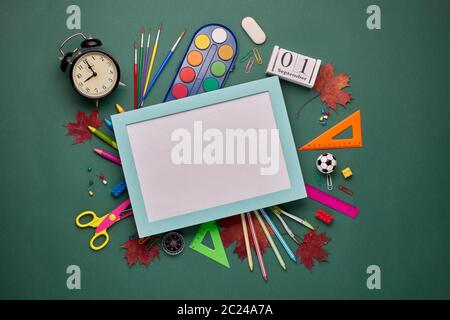 Cornice blu con foglio bianco e accessori di cancelleria: Matite, penne, altri materiali per ufficio su sfondo verde. Vista dall'alto, spazio di copia. Accesso alla scuola Foto Stock