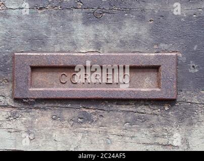 una vecchia letterbox in ferro arrugginito in una porta di legno nero con vernice spellante con la parola correio Foto Stock