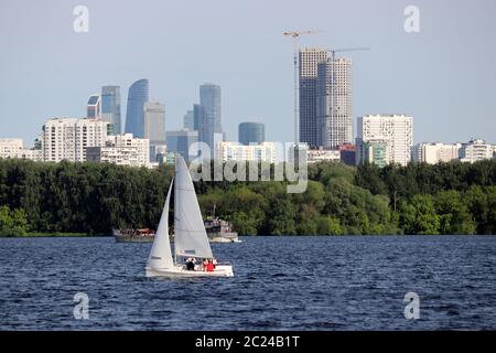 Vista sulla città in estate dal fiume Mosca. Barca a vela e windsurf sullo sfondo di un parco verde e grattacieli residenziali Foto Stock