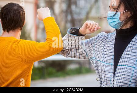 Urto del gomito. Coronavirus, malattia, quarantena, maschera medica, COVID19. Saluto di coppia con gomiti. I gomiti si sono urtare. Amici in maschera medica protettiva su Foto Stock