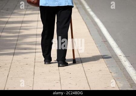 Donna che cammina con un cane su una strada, gambe femminili sul marciapiede. Concetto di disabilità, di dimagrire, di malattie della colonna vertebrale, di anziani Foto Stock