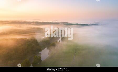 Estate natura paesaggio panorama dell'antenna. Nebbia di mattina su fiume, prato e bosco. Una natura che stupisce la luce del sole di scena a foggy sunrise. La Bielorussia, Europa Foto Stock