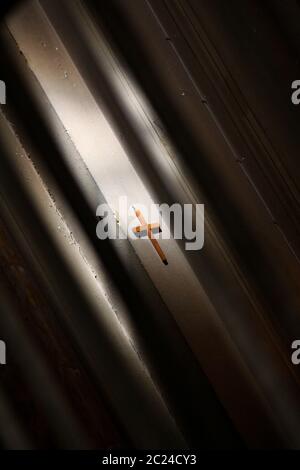 Semplice croce di legno appesa alla parete con gioco di luce e ombra Foto Stock