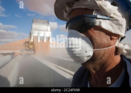 Un lavoratore usa un facemask contro la polvere mentre la sabbia viene versata su forme concrete in lavori per costruire un grande impianto petrolifero nel deserto del Sahara. Foto Stock