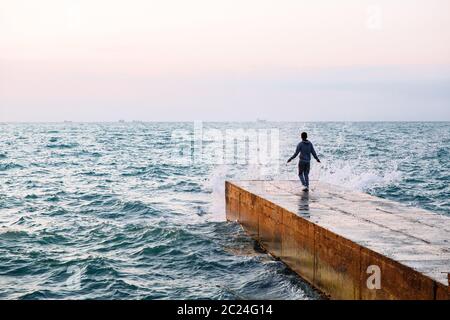 Lunghezza piena vista del giovane sportivo del salto con la corda, allenamento sul molo, vicino al mare. Vista dal retro. Foto Stock