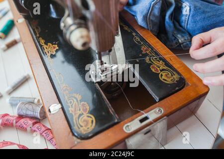 Closeup di mano femmina che cambia filo su vecchia macchina da cucire a casa Foto Stock