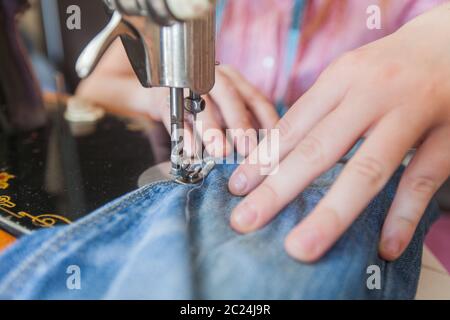 casalinga che ripara jeans blu con macchina da cucire d'epoca retrò a casa Foto Stock