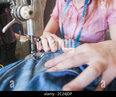 casalinga che ripara jeans blu con macchina da cucire d'epoca retrò a casa Foto Stock