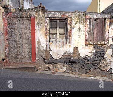 una vecchia casa in rovina in parte crollò su una strada con una porta bloccata che si sgretolava le pareti e sbiadisce le finestre dipinte di rosso con clos Foto Stock