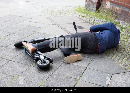 Inconscio uomo disteso sul cemento Street dopo un incidente con uno scooter elettrico Foto Stock