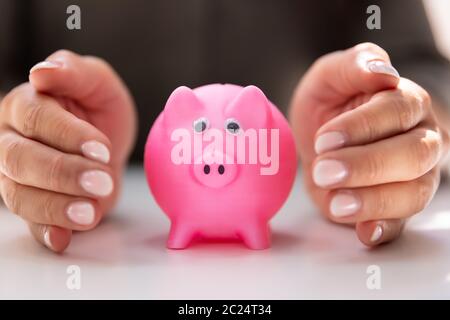 Close-up di una mano umana proteggere Rosa Salvadanaio sulla scrivania bianca Foto Stock