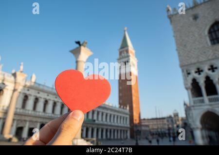 Mano che tiene il cuore di fronte alla Torre della Basilica di San Marco in Piazza San Marco Foto Stock