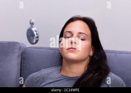 Attraente giovane donna essendo ipnotizzato comodamente seduti sul divano di casa Foto Stock