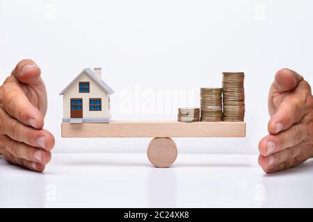 Primo piano della casa modello e monete in equilibrio su legno scala di pesatura Foto Stock