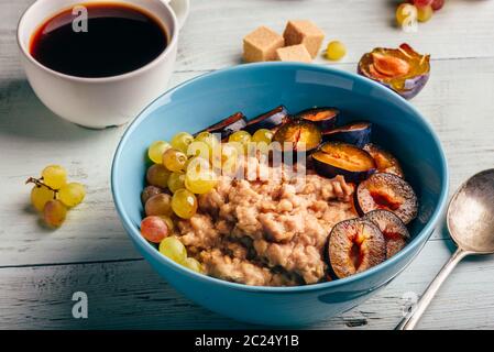 Colazione sana nozione. Porridge con prugna fresca, verde UVA e la tazza di caffè. Foto Stock