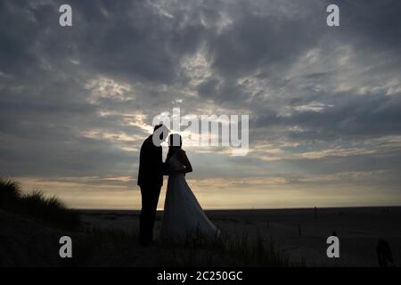 Silhouette di sposa e di sposo abbraccianti sulla spiaggia serale. Cielo nuvoloso sullo sfondo. Felicità, amore, concetto di fiducia. Foto Stock