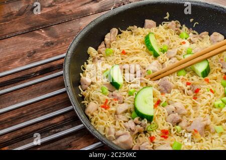 Tagliatelle cinesi con pollo in padella e tavolo in legno Foto Stock