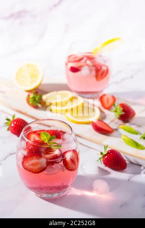 Gin freddo rosa al gusto di fragola e tonico guarnito con frutta fresca, foglie di limone e menta. Foto Stock