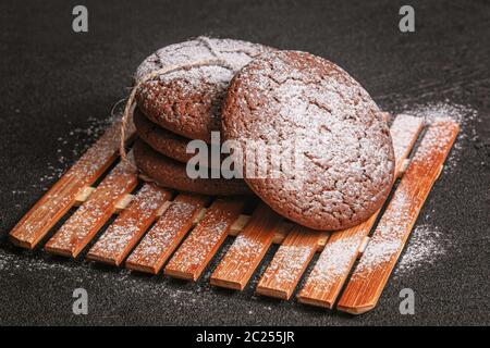 i biscotti di porridge di cioccolato legati con una corda cosparsa di zucchero in polvere giace su una piastra di bambù su cemento nero Foto Stock