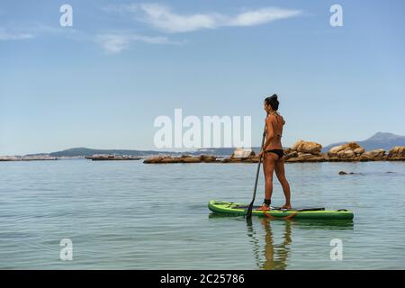 Donna che fa sport d'acqua di paddle surf in mare Foto Stock