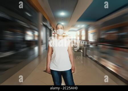 Ragazza in maschera protettiva cammina in un centro commerciale vuoto senza persone e negozi chiusi. Eliminazione parziale delle restrizioni di quarantena dopo la pandemia del coronavirus Covid-19, fuoco selettivo Foto Stock