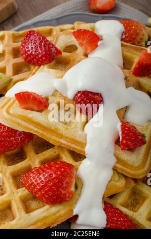 Waffle fatti in casa con sciroppo d'acero e fragole, crema fresca in cima, bevanda fresca all'arancia Foto Stock