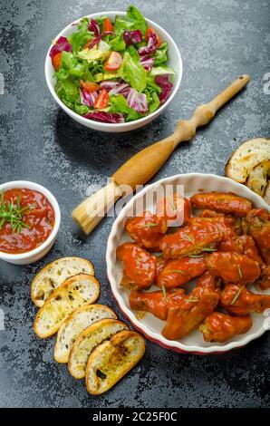 Hot ali di pollo con il piccante salsa habanero e insalata mista con pomodorini e grigliate di baguette con olio d'oliva Foto Stock