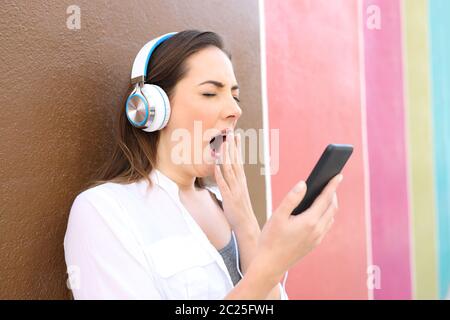 Donna annoiati sbadigli utilizzando smart phone e le cuffie per ascoltare la musica in un colorato street Foto Stock